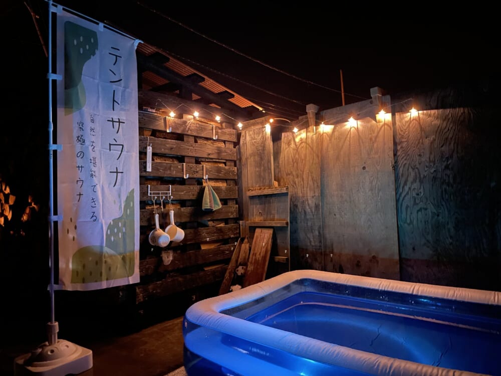 暖色のキャンプライトとテントサウナののぼりがある夜の水風呂スペース